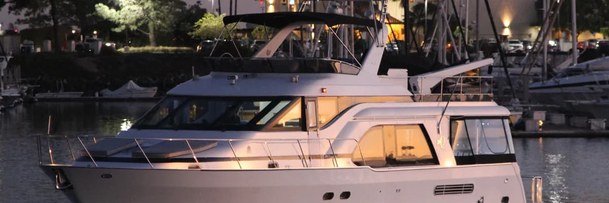 A flybridge motor yacht photographed at dusk, her saloon lit from within