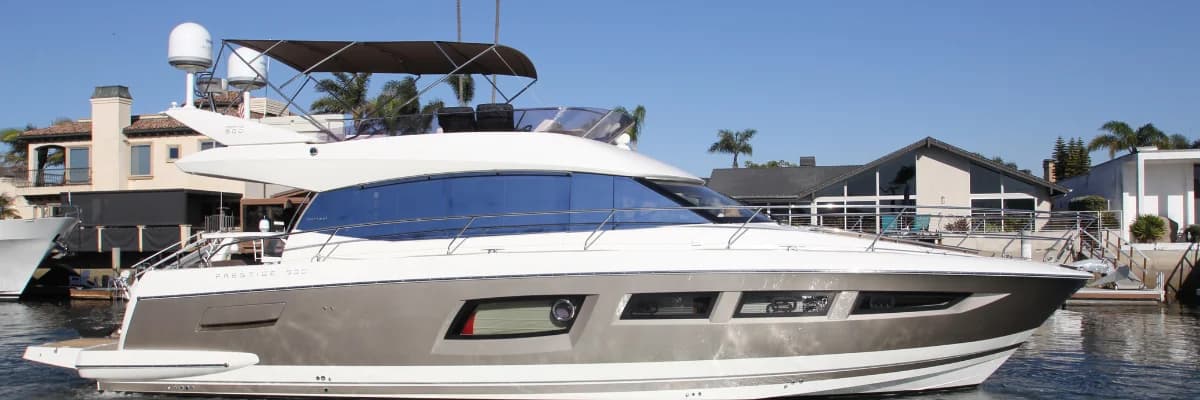 A flybridge motor yacht with a champagne hull moored along a residential canal